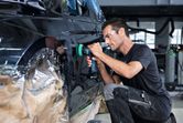 A person wearing safety equipment polishes a car door with a cordless tool.