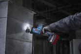 A person wearing safety equipment cuts sheet metal with a cordless reciprocating saw.