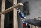 A person wearing safety equipment uses a reciprocating saw to cut wooden beams.