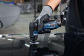 A person wearing safety equipment sands a metal surface with a compact orbital sander.