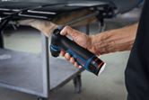 A person holds a cordless orbital sander near a metal workbench.