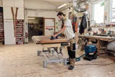 A person wearing safety equipment sands a wooden surface with a cordless random orbit sander.