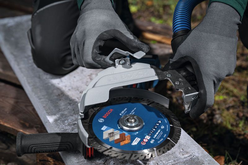 A person wearing safety equipment attaches a dust extraction guard to a large angle grinder.