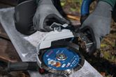A person wearing safety equipment attaches a dust extraction guard to a large angle grinder.