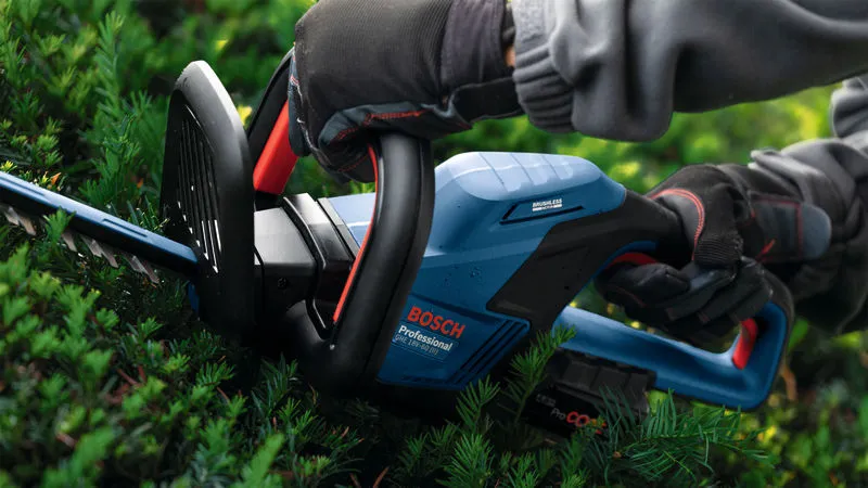 A person wearing safety equipment trims hedges with a cordless hedgecutter.