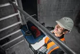 A person wearing safety equipment mounts a cordless jobsite light to a metal pipe.