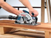 A person uses a hand-held circular saw with dust extraction to cut a wooden plank.