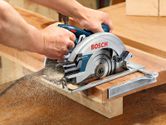 A person uses a hand-held circular saw to cut through a wooden plank.