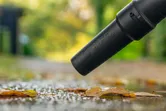 Cordless leaf blower clearing wet leaves from a path after rain.