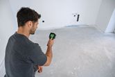 Person operates a thermo camera to inspect temperature variations on a bare floor.