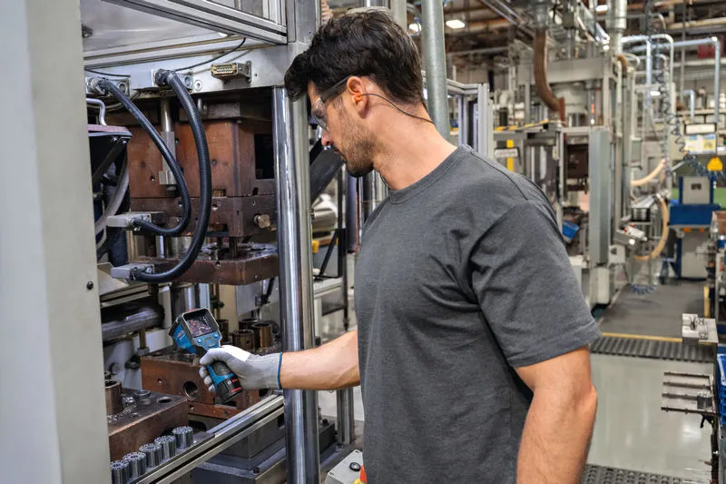 A person wearing safety equipment inspects machinery using a thermo camera.