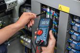 Person measures voltage on electrical panel using a digital multimeter.