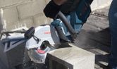 A person wearing safety equipment cuts a concrete block with a cordless grinding saw.
