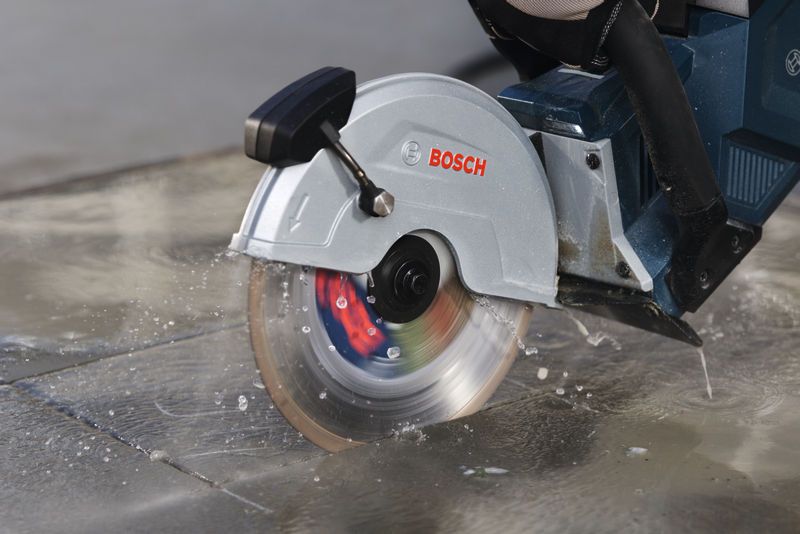 Cordless cut-off saw slicing wet concrete outdoors.