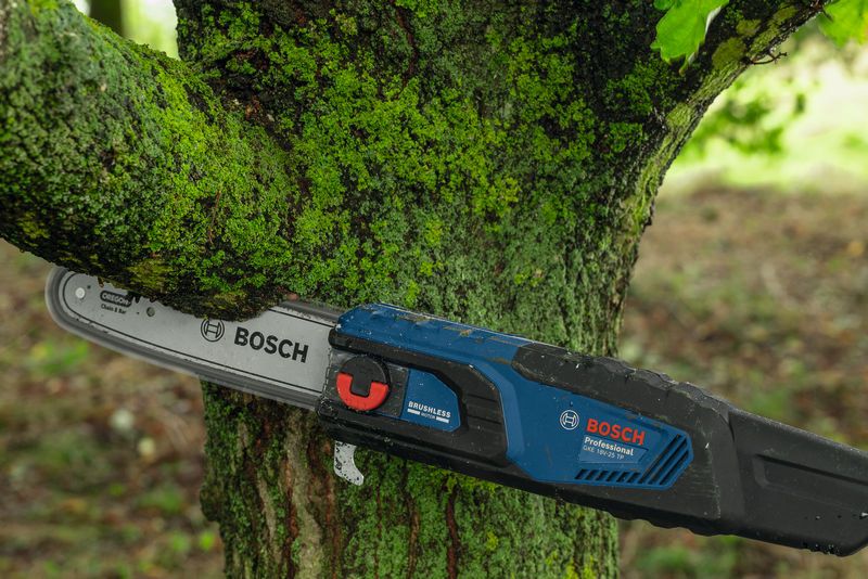 Electric chainsaw cutting through a mossy tree branch outdoors.