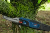 Electric chainsaw cutting through a mossy tree branch outdoors.