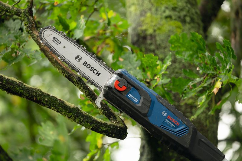 Cordless pole saw trimming a tree branch outdoors.
