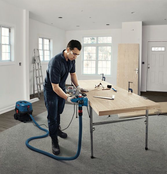 A person wearing safety equipment uses a planer on a wooden board in a workshop.