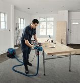 A person wearing safety equipment uses a planer on a wooden board in a workshop.