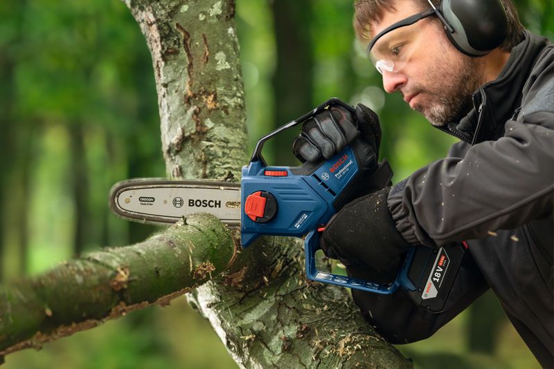 A person wearing safety equipment trims a tree branch with a cordless pruner saw.