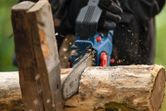 A person wearing safety equipment uses a cordless pruner saw to cut a log.