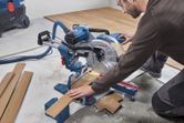 A person wearing safety equipment cuts wooden flooring with a sliding mitre saw.