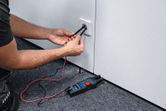 Person uses a fork meter to measure voltage at an electrical outlet.
