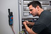 A person checks electrical wires in a control panel using a digital multimeter.