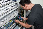 A person tests electrical wires in a control panel using a fork meter.