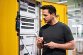 A person tests a component at an open electrical panel with a digital multimeter.