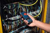 A person uses a clamp meter to measure current in an electrical control panel.