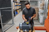Person testing an industrial motor with a clamp meter in a warehouse.