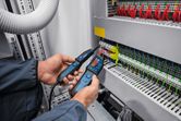 Person wearing safety equipment uses a voltage tester on an electrical panel.