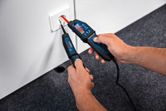 Person tests an electrical outlet with a voltage tester on a carpeted floor.
