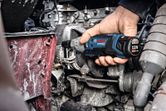 A person uses a cordless ratchet wrench to fasten a bolt in an engine compartment.