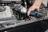 A person uses a cordless ratchet wrench to tighten a bolt inside a car engine.