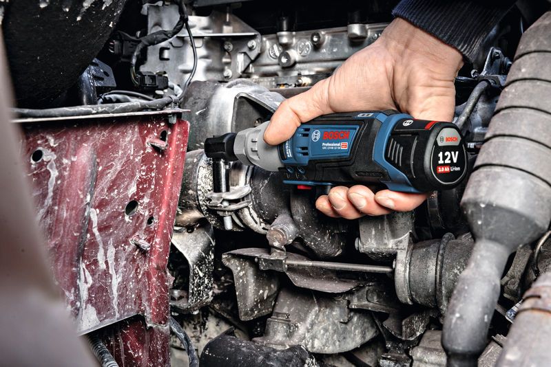 A person uses a cordless ratchet wrench to tighten a bolt on an engine.