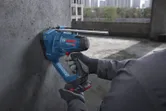 A person wearing safety equipment cuts a threaded rod against a concrete wall.