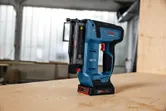 Cordless nail gun standing upright on a wooden table in a workshop.