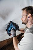 A person wearing safety equipment uses a power tool to fasten material to a wall.