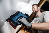Person wearing safety equipment uses a cordless nail gun to fasten material to a ceiling.