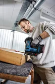 A person wearing safety equipment uses a cordless nail gun to fasten wooden joints.