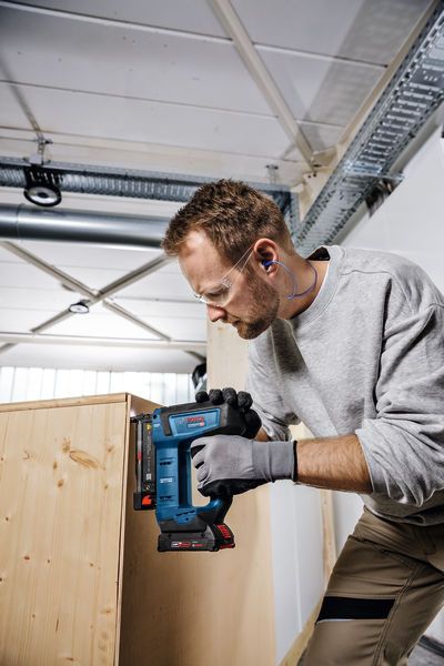 Person wearing safety equipment uses a jigsaw to cut wood in a workshop.