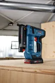 Cordless electric nail gun resting on a wooden surface in a workshop.