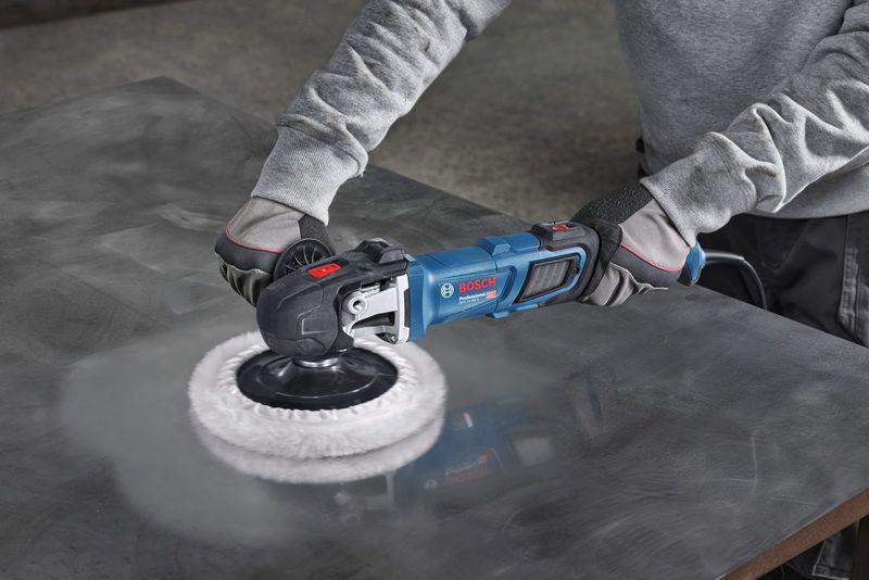 A person wearing safety equipment polishes a metal sheet using a power polisher.