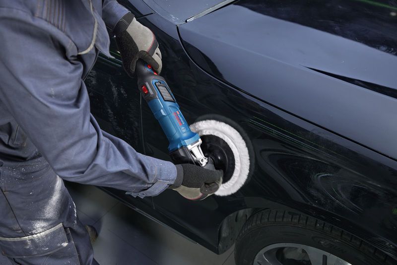 A person wearing safety equipment polishes a car door using a power polisher.