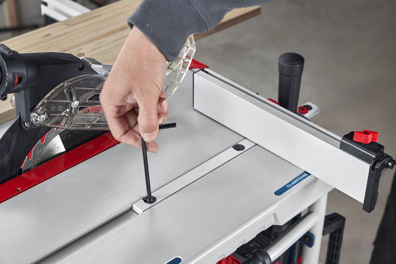 Person adjusts a table saw with an Allen key while preparing to cut wood.