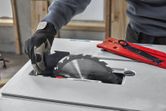 A person wearing safety equipment adjusts a table saw blade with a tool nearby.