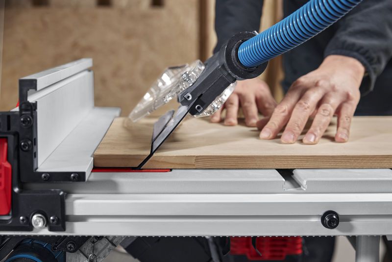 A person pushes wood through a table saw with dust extraction in a workshop.