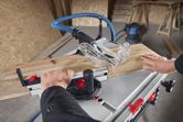 A person pushes wood through a table saw in a workshop.
